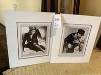 Both framed photos shown leaning against wall on carpet, visible signatures and white double mats.
