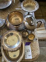 Full display of sterling and silver plated items including baby cup, tea pot, and various dishes.