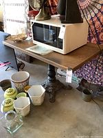 Table with microwave and decorative items on and around it showing wooden top and wrought iron base.
