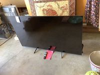 Full view of the TCL television showing the black screen and stand legs on a concrete floor.