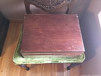 Closed rosewood box on green cushioned chair, showing vintage wooden storage box for silverware.