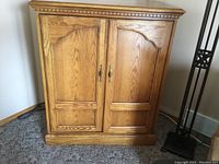 Solid oak TV cabinet front view showing doors, carved trim, and brass handles.