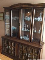 Wooden china cabinet with glass doors and displayed crystal ware, ornate carved wood base with metal handles.