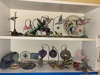 Full view of two shelves displaying glass birds, pottery, glass balls, butterflies, and geodes.