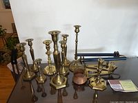 Photo showing all brass candlesticks and two wall sconces arranged on a table with some accessories including candle snuffers.