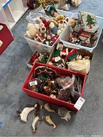 Wide view of bins and boxes containing various Christmas decorations including plush figurines, wood ducks, mini wreaths and other items packed together
