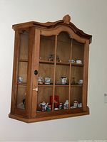 Front view of the wood display cabinet with glass door and contents inside including miniature tea cups and collectibles.