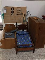 Wooden doll cradle and bed with blue cushions and polka-dotted mattress, plus brown case containing dollhouse furniture