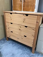 Front view of unfinished wooden dresser with three drawers, showing natural wood grain and minimalistic cutout handles.
