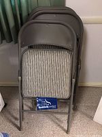 Photo of four stacked padded folding chairs with visible striped fabric seats and Sudden Comfort label on one chair.