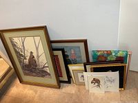 Group photo showing multiple framed and unframed prints leaning against a wall, including a large framed bird print (John A Ruthven grouse) and colorful fabric art on right