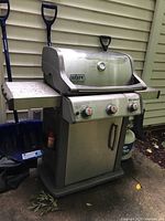 Front view of stainless steel Weber Spirit grill with side shelf and propane tank
