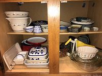 View inside cabinet showing assorted kitchen bowls, ramekins, covered baking dishes, glass bakeware, and measuring cups