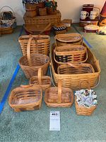 Photo shows ten Longaberger baskets arranged on carpet. The baskets vary in size and shape, mostly rectangular with handles, and one with fabric liner.