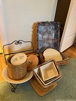 Overview of several Longaberger baskets, including one with lid, multiple ceramic dishes in basket, and metal stand