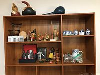 Wide shelf view showing maracas, warrior figurines, ceramic pieces including salt and pepper shakers, dolls, and miniature rocking chair