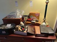 Photo showing four men's watches stored in a display case, various wallets, jewelry boxes, two clocks, shaving brushes and razor on wooden furniture.