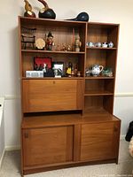Front view of the two-piece teak bar cabinet with shelves displaying assorted items and closed sliding doors.