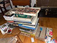 Stack of board games and puzzles including Clue, 1000-piece puzzles, and several game boxes, plus wooden peg solitaire and sliding puzzle game boards on floor.
