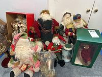 Photo showing multiple Santa Claus figurines including one in a green box, arranged together with some seated and some standing.