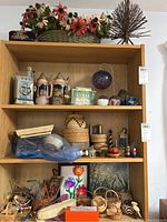 Full view of wooden shelving unit showing all items including beer steins, liquor bottles, glass paperweights, baskets, miniature dolls, and artwork at the bottom