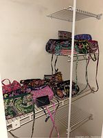 Angle overview of several Vera Bradley zipper bags on white wire shelving, showing assortment of colorful patterned bags.