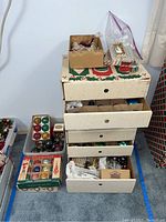 Stack of four cardboard drawers containing various boxed and loose ornaments, plus plastic storage bins at floor level