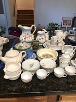 Overview of porcelain tea service, pitchers, cups, saucers, and bowls arranged on a countertop