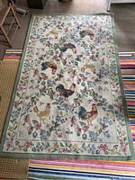 Full view of the 5x8 wool rug featuring roosters, hens, and floral motifs with a green border on a cream background.