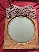 Full view of the antique round beveled mirror in a golden oak frame with decorative carved scrollwork on top.