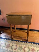 Side view of the table with one drop leaf closed showing turned legs and natural wood finish