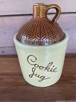 Outer view of the cookie jar showing beige base with 'Cookie Jug' inscription and brown jug-shaped lid with handle and spout.