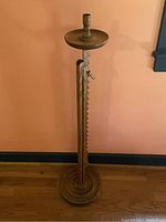 Full height view of the oak adjustable candle holder stand against a wall.