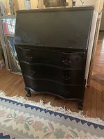 Closed black painted mahogany slant-top desk with three front drawers and ball and claw feet.