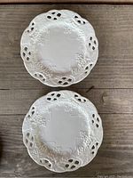 Top view of two white milk glass plates showing embossed grape and vine pattern and pierced edges