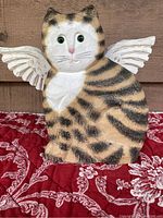 Front view of hand carved wooden cat with wings, striped pattern, green eyes, and pink nose