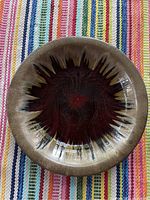 Top view of large round ceramic bowl showing color gradation from red center to brown rim on a multicolor striped surface.