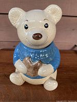 Front view of ceramic bear cookie jar, showing bear's smiling face, blue sweater, and cookie in hands.
