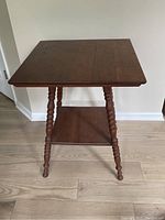 Full front view showing square wooden top and four turned legs connected by a lower shelf.