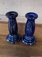 Pair of cobalt blue ceramic candlesticks on wooden surface against grey wall.