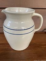 Front and side view of the cream-colored stoneware pitcher with two blue bands, showing shape and handle.