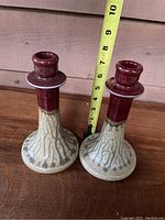 Two ceramic candleholders side by side with measurement tape showing height of approximately 8 inches