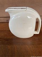 Side profile of the white ceramic pitcher showing curved handle and gold-trimmed lid