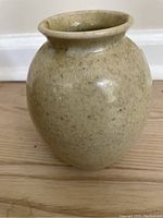 Front view of the beige speckled pottery vase showing rounded body and flared rim.