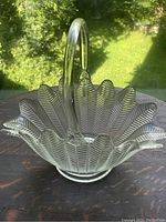 Clear glass basket showing textured herringbone leaf patterns, scalloped edge, and arching handle on natural light background.