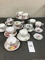 Photo showing 13 assorted floral porcelain teacups and saucers arranged in groups highlighting diverse flower patterns and gold trims.