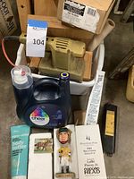 Shows Black & Decker finishing sander, Cheer liquid laundry detergent, bobblehead with box, and Bliss body butter tube on concrete floor.