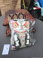 Three cushions grouped: two batik-style cushions and one Day of the Dead cat cushion in plastic bag.