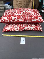 Two lumbar-style cushions stacked, showing red damask floral pattern on white background, measuring about 20 inches width.