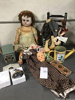 Photo of the large scary doll in yellow dress, small doll, chair with witch doll, pillow, outfit, decorative watering can, and certificate with collectibles.